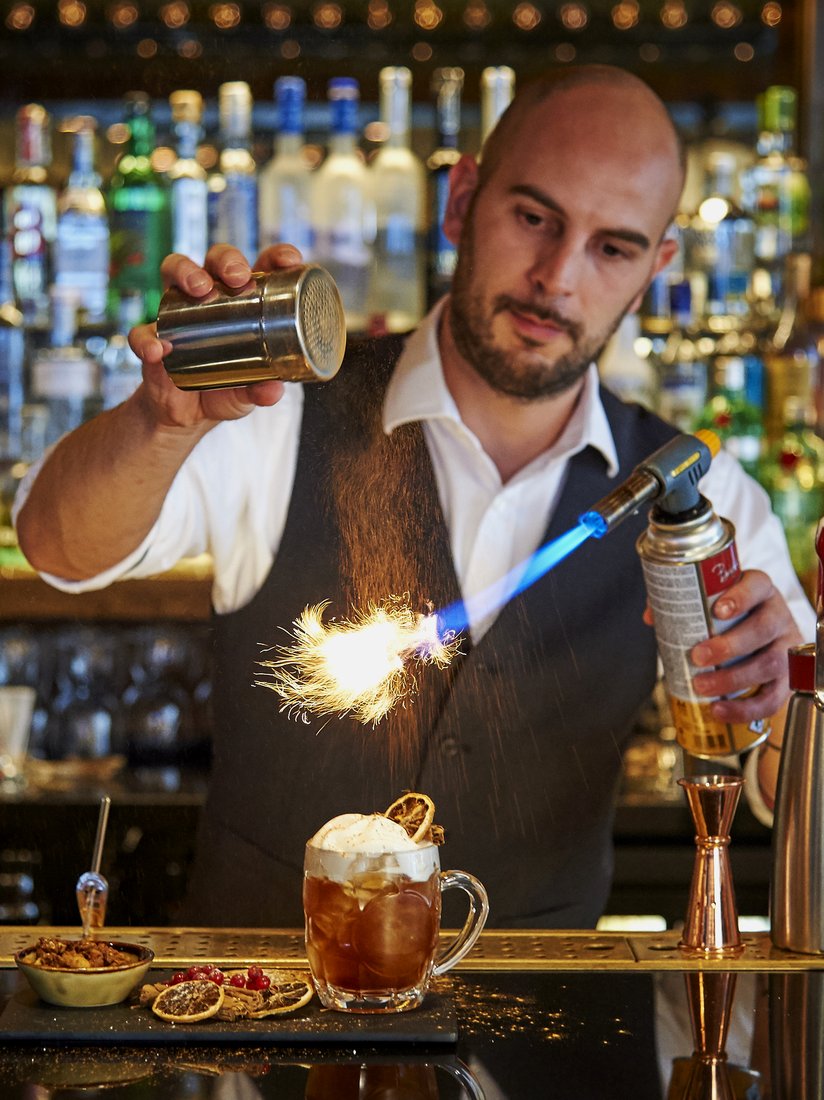 Salute bartender flaming a garnish over a cocktail